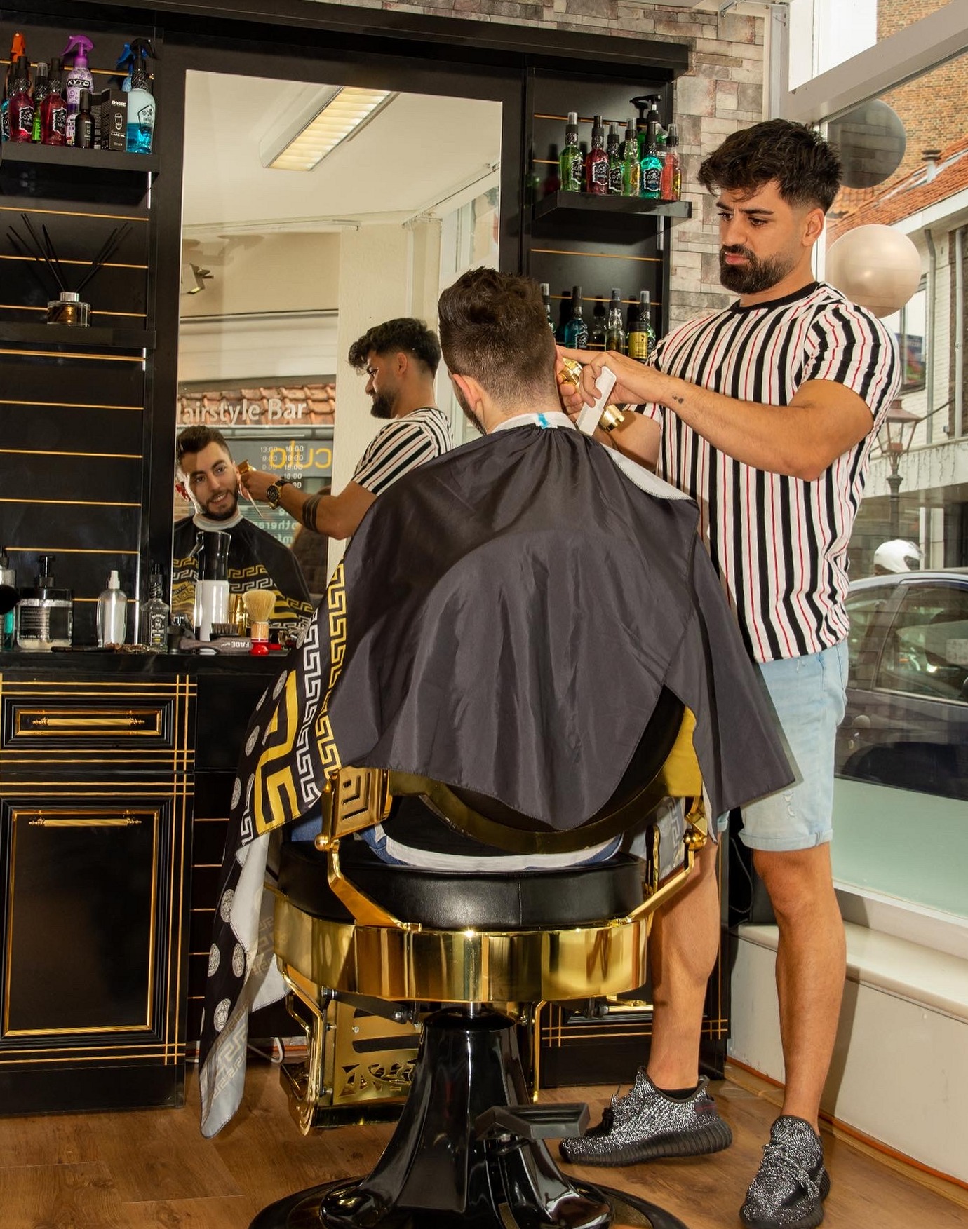 Twee kappers in Hairstyle bar bij de zwart met gouden kappersstoel voor de spiegelwand