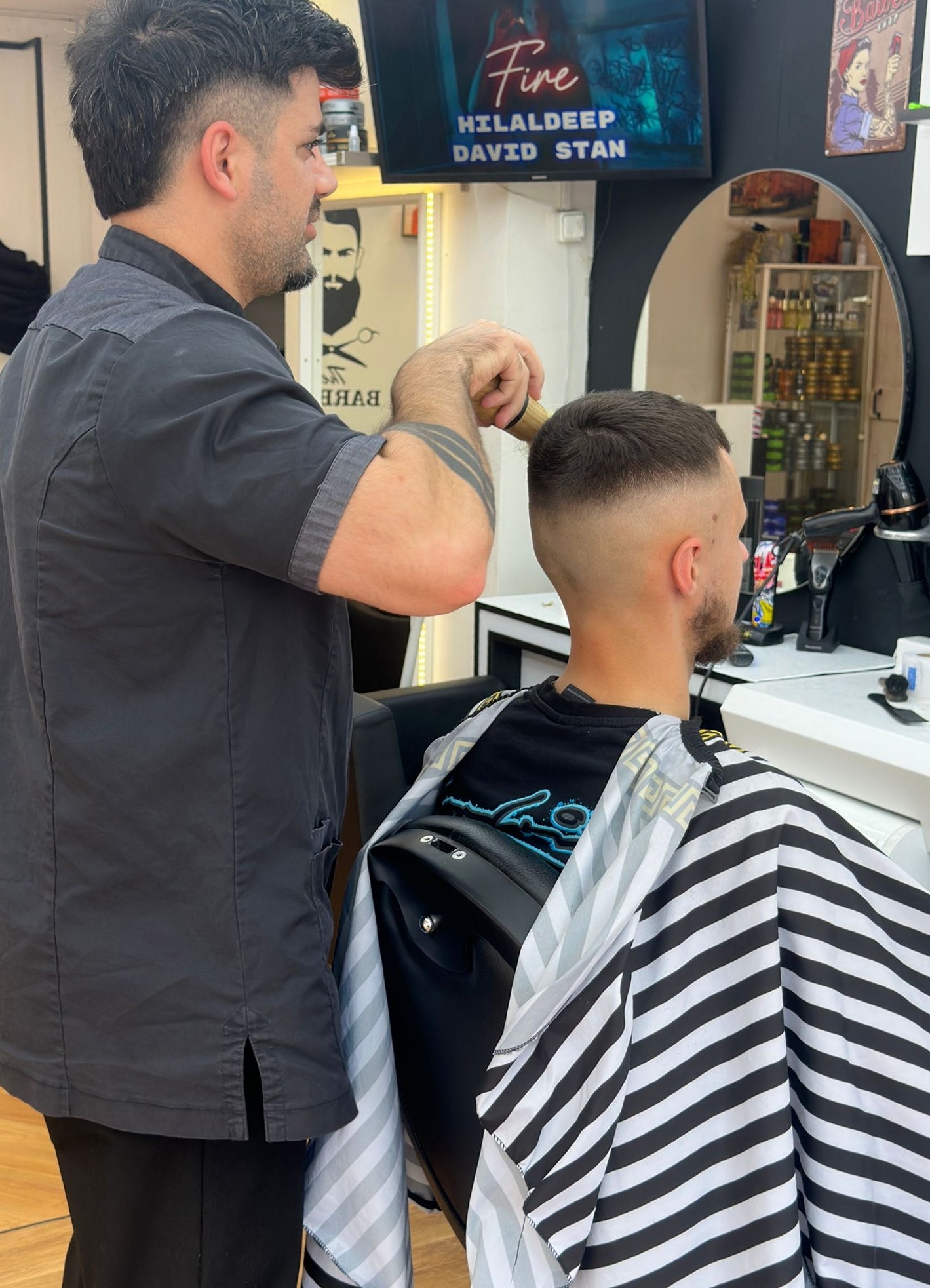Een kapper van Hairstyle bar maakt een kort kapsel af bij een klant in een gestreepte kapmantel